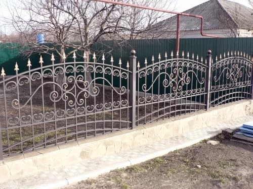 Traditional ornamental iron fence with scrollwork and pointed finials above a stone wall